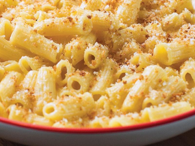 Creamy baked mac n' cheese with bread crumbs placed on a white plate with a red trim