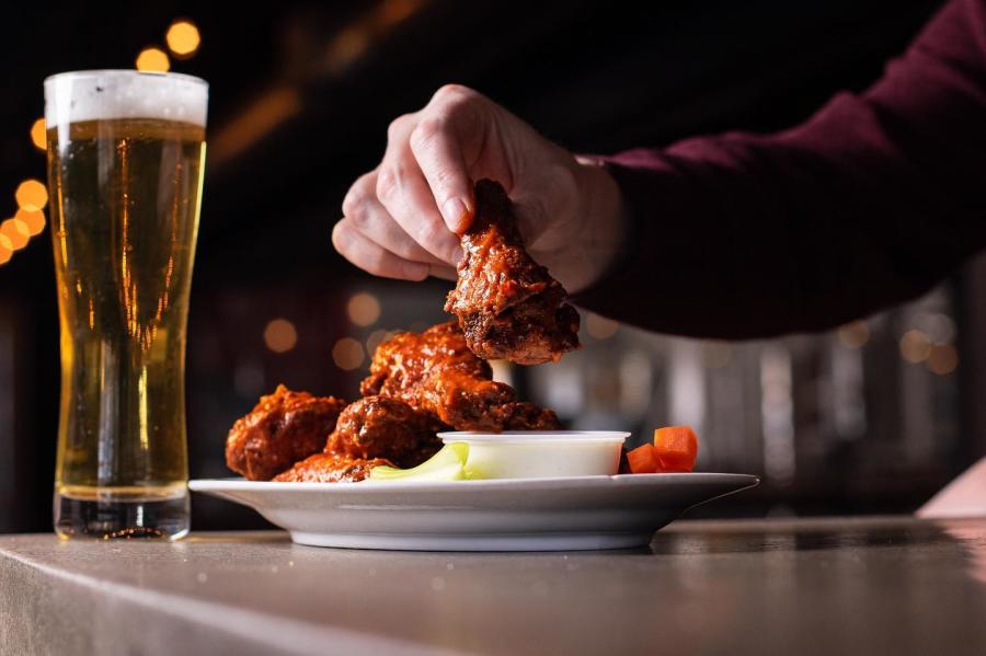 Someone picks up a wing from a large plate with a beer in front of them at Rio Bravo Brewing Company