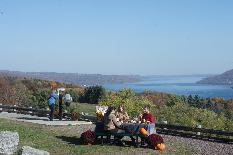 Women having a picnic and woman looking through a viewfinder in Carolabarb Park with panoramic views of Lake Canandaigua.