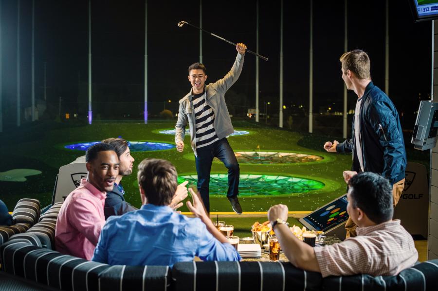 A man celebrates his shot with a group of friends at TopGolf