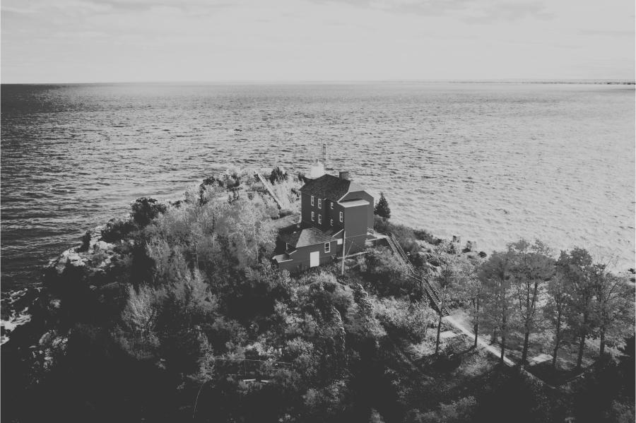 A black and white aerial photo of the Marquette Harbor Lighthouse overlooking a vast Lake Superior