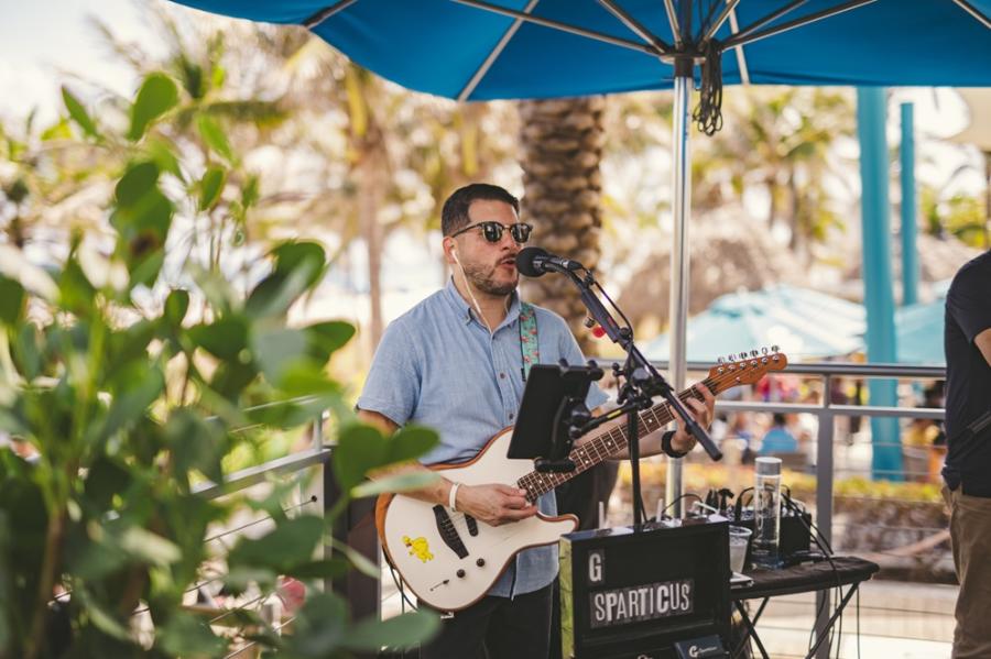 Man playing a guitar under a blue umbrella on the patio of Oceanic