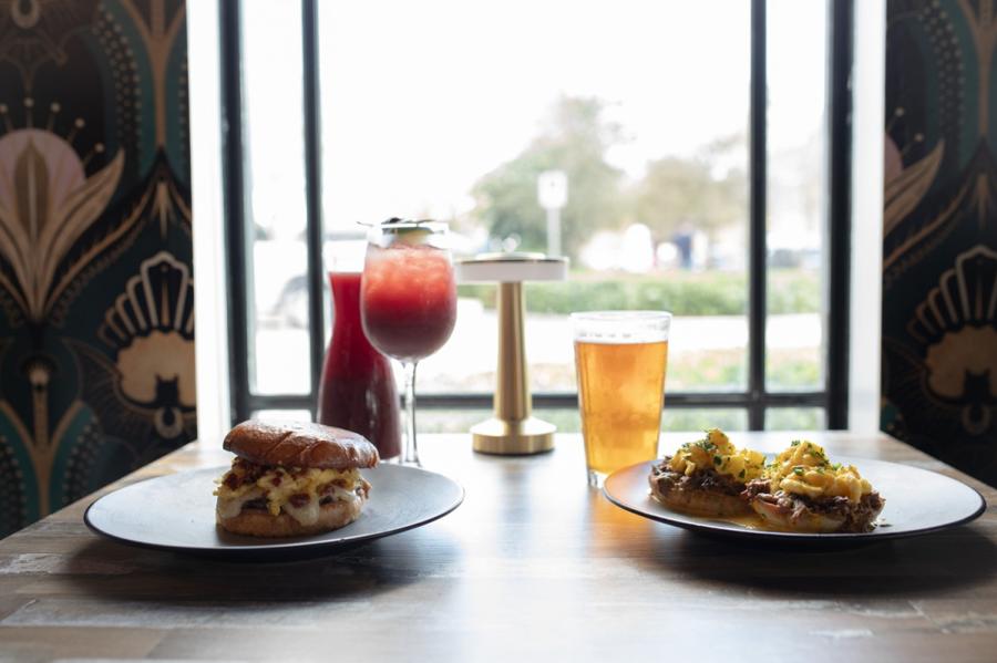 Two breakfast sandwiches, a carafe of Sangria and a pint of beer, set on a table in front of a window at The Vault in Pompano Beach, FL