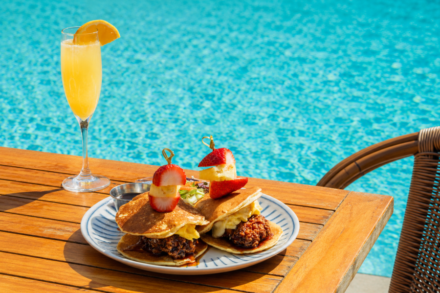 Two Pancake Korean Chicken Sliders with a Mimosa set on a table by the pool at Lola's By The Water in Pompano Beach, FL.