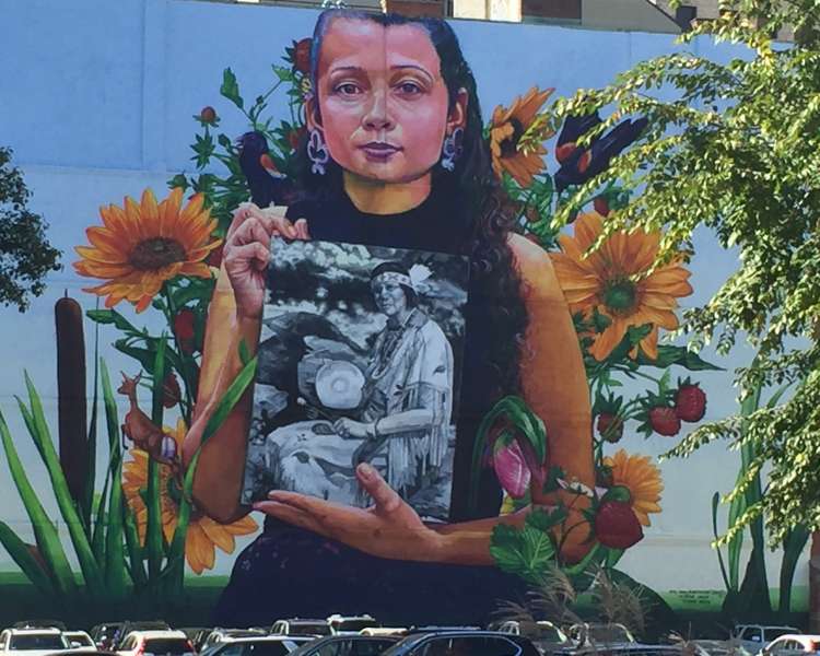 Mural (2018) depicting a member of the Narragansett Indian Tribe holding a photo of Princess Red Wing, a Narragansett/Pokanoket-Wampanoag elder who founded the Tomaquag Museum (Exeter).  Located at 32 Custom House Street.