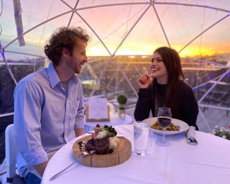 A couple dining in a rooftop igloo at sunset.