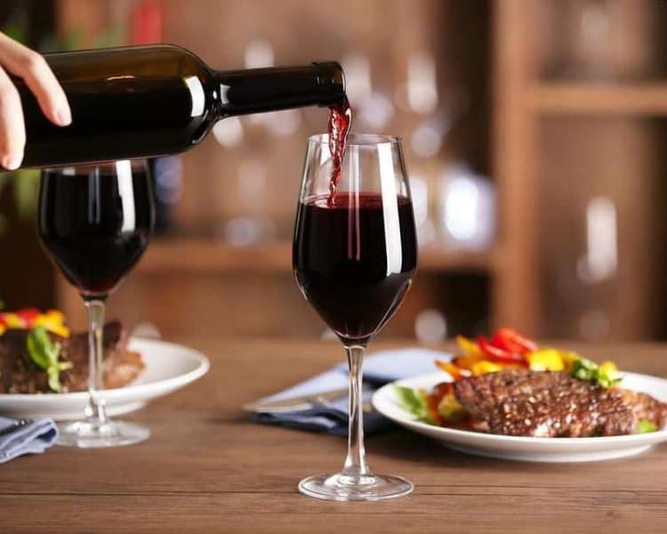Hand pouring red wine for two, with two entrees on the table.
