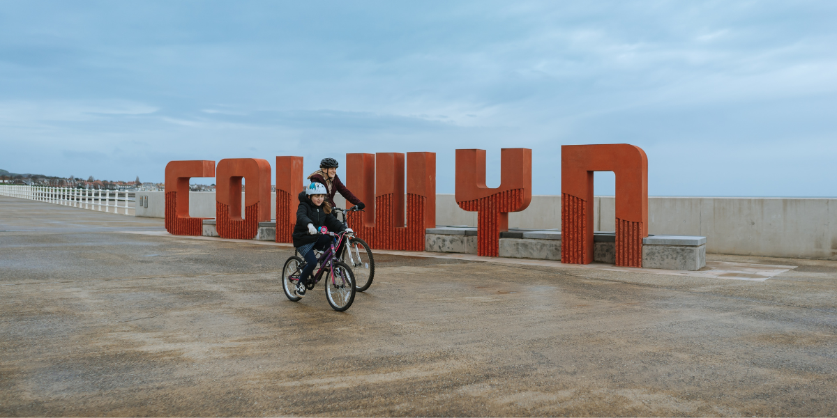 Cyclists going past the Colwyn sign