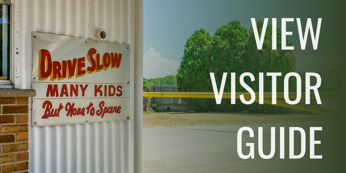 Entrance to Getty Drive-In with sign that reads "drive slow, many kids but none to spare" on side of ticket booth. to the right text reads View Visitor Guide