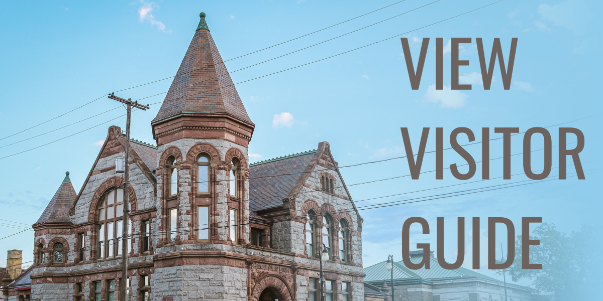 roof peaks and arched windows of historic stone library in richardsonian romanesque style set against blue sky. to  the right text reads view visitor guide