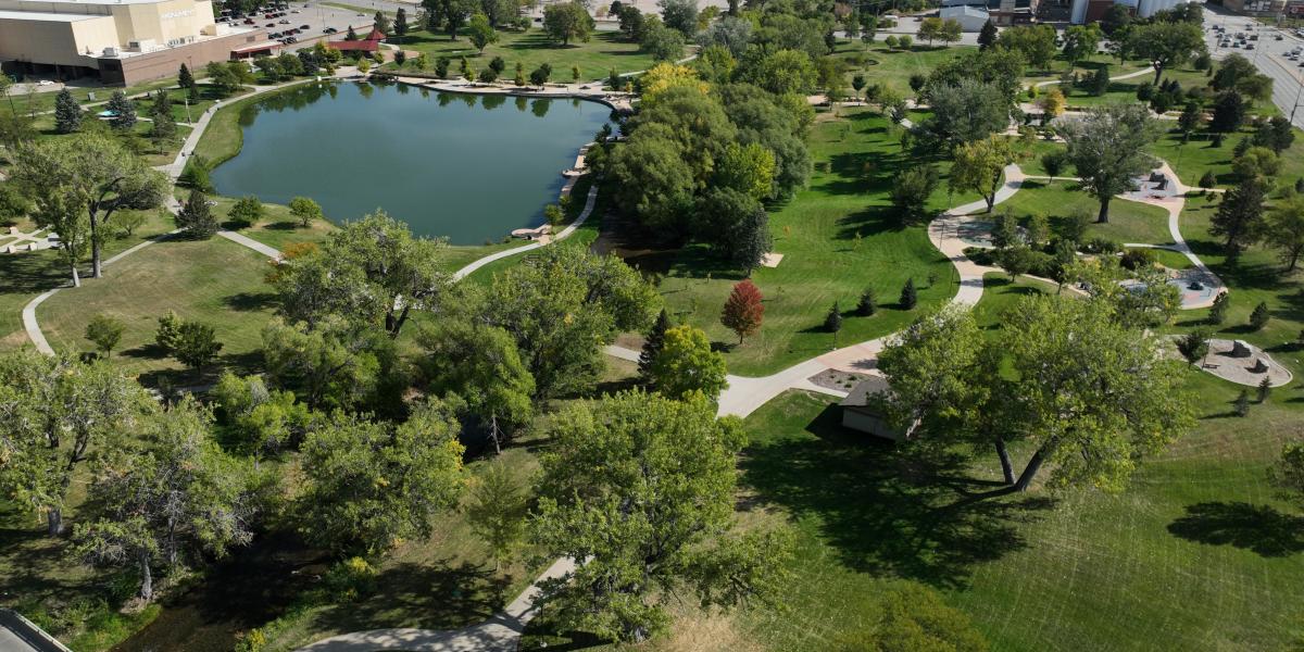 Aerial view of Memorial Park with a central pond surrounded by green lawns and pathways. Tall trees dot the landscape, evoking a calm, peaceful atmosphere.