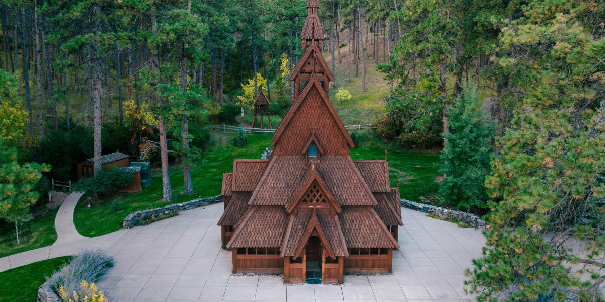Aerial view of Chapel in the Hills, with steep gabled roofs in a lush forest setting. The earthy tones contrast with vibrant green trees, creating a serene, historic ambiance.