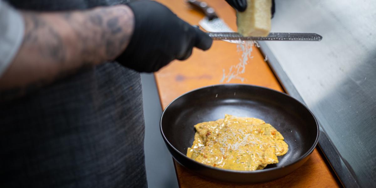 A chef grates cheese over a creamy pasta dish in a black bowl, creating a gourmet and refined presentation.