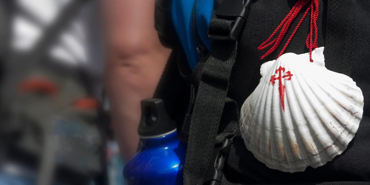 Person with Camino shell tied with a red string to back of rucksack