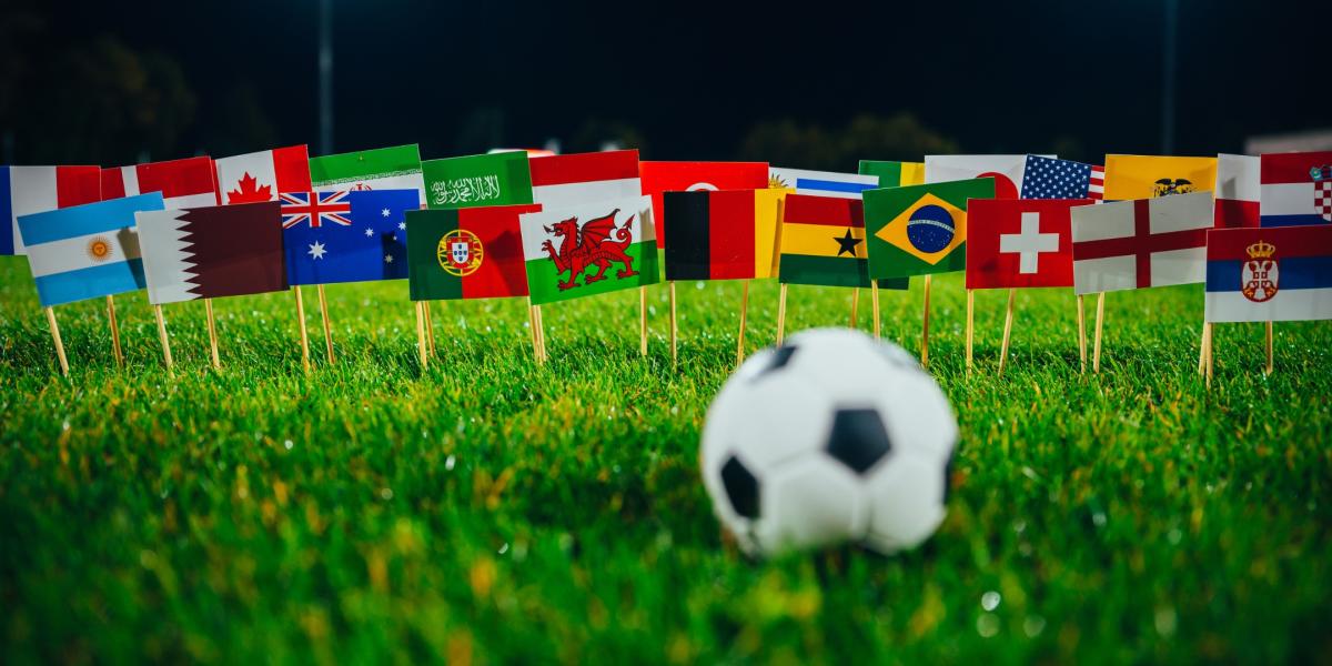Football on grassy field in front of collection of flags of the world including England, Wales, Portugal, Germany and more