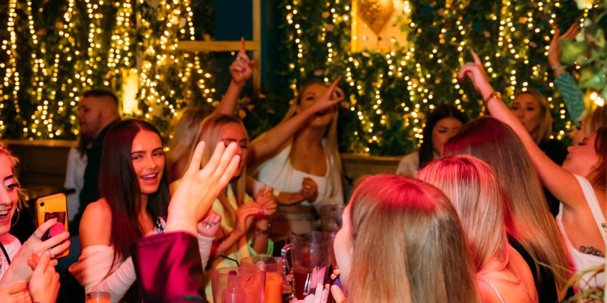 Group of women toasting their drinks at brunch at Funky Flamingo surrounded by fairy lights