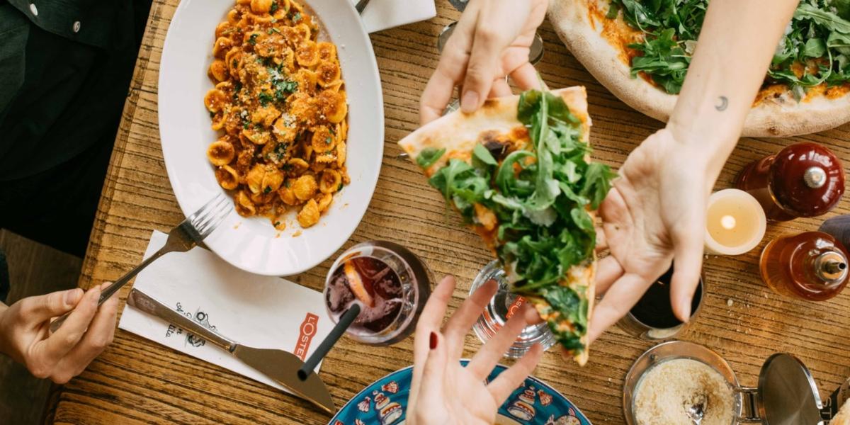 L'Osteria group sharing veggie pizza and pasta dishes around table
