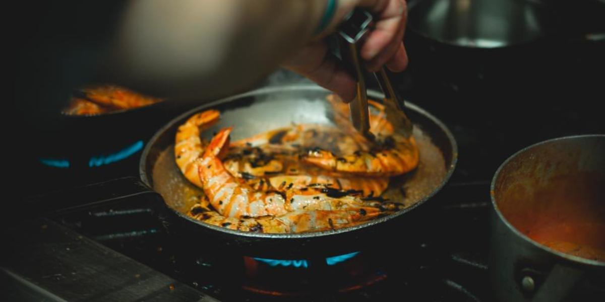 Chef cooking shrimp in hot frying pan on stove top at Max's Brasserie