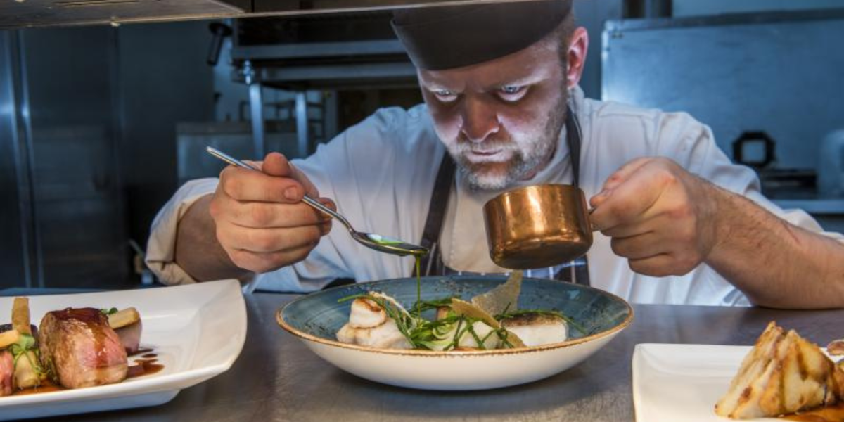 Male Chef carefully platting up dish, drizzling sauce across blue bowl at The Blue Room restaurant
