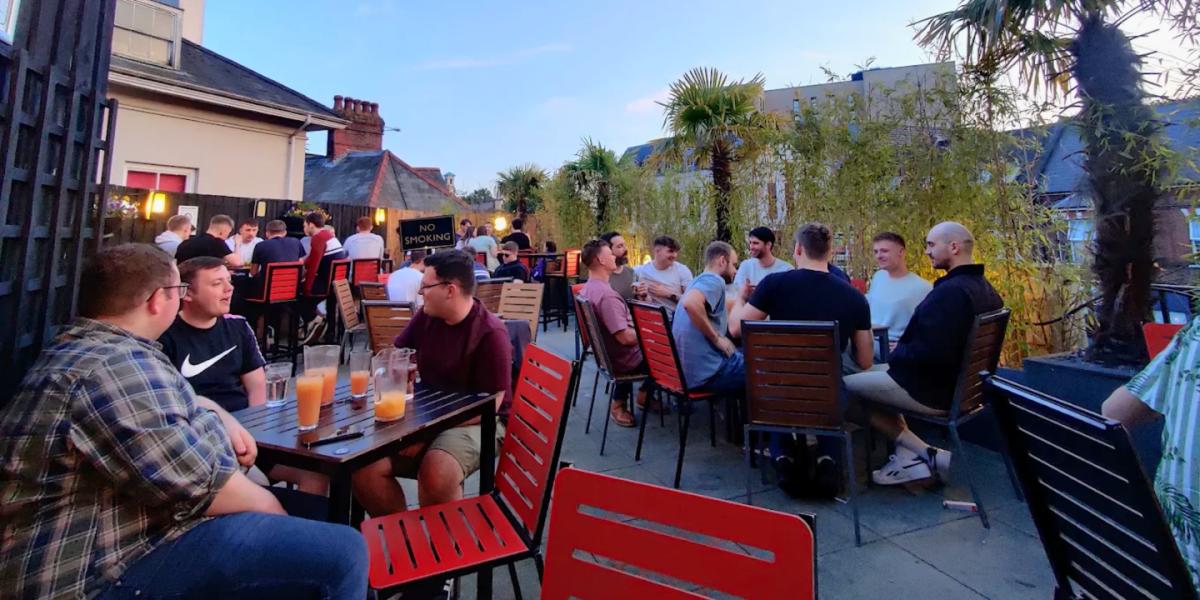 Groups of people sat around tables with drinks at The Giddy Bridge rooftop terrace