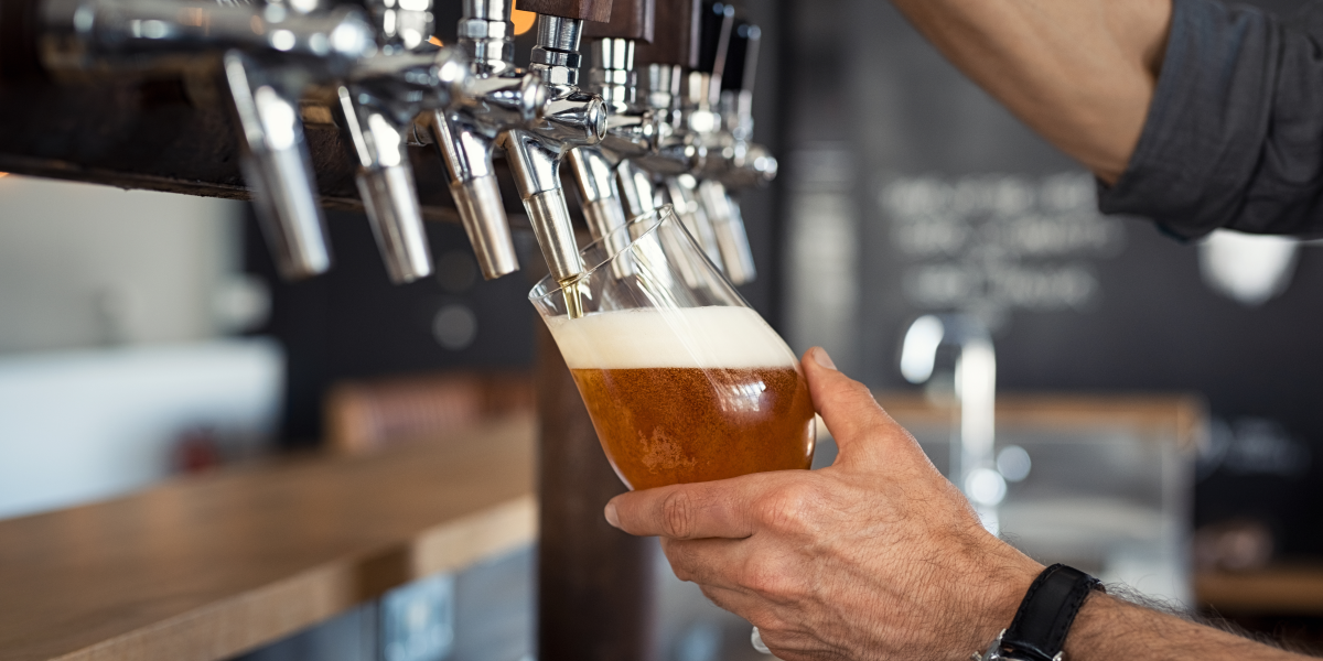 Bartender pouring craft beer from tap into glass at Wausau bar with foamy head, stainless steel taps, and wooden counter setting.