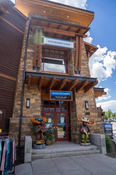 Stone building with wooden accents features a welcoming entrance. Colorful moose sculptures flank the door, promoting local attractions.