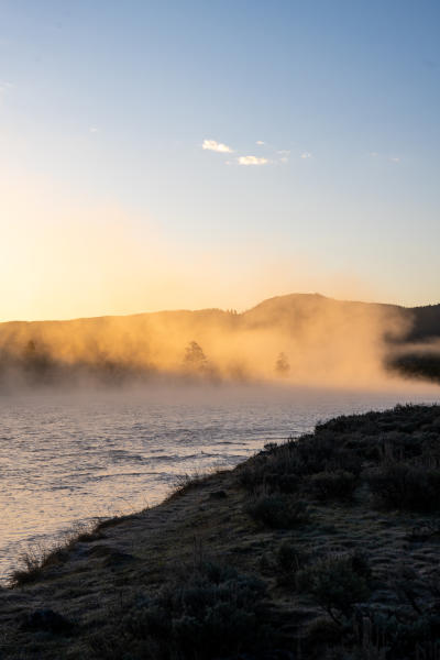 Mist rises above a river with golden light fading through.