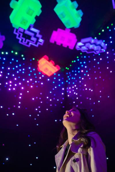 Woman looking up admiring colorful LED Space Invaders inside Otherworld exhibit