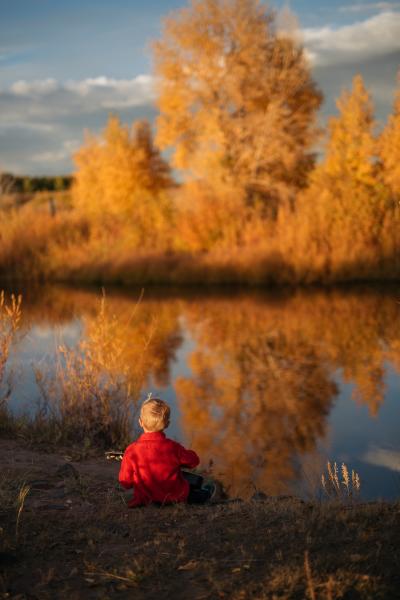 boy playing guitar beside river in fall