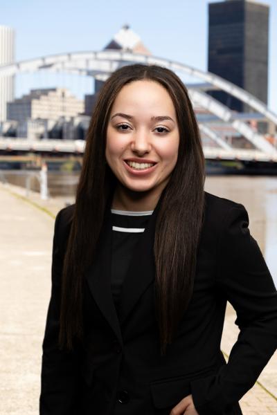 Woman standing in front of bridge in downtown Rochester wearing a black blazer with hand in her pocket
