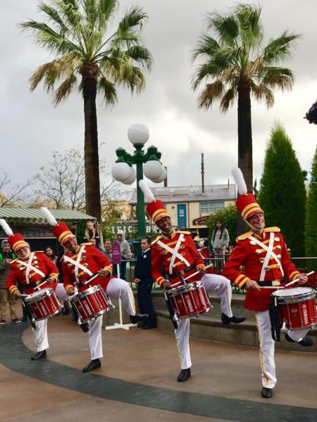 Four people have dressed to look like toys, all holding and playing the drums.