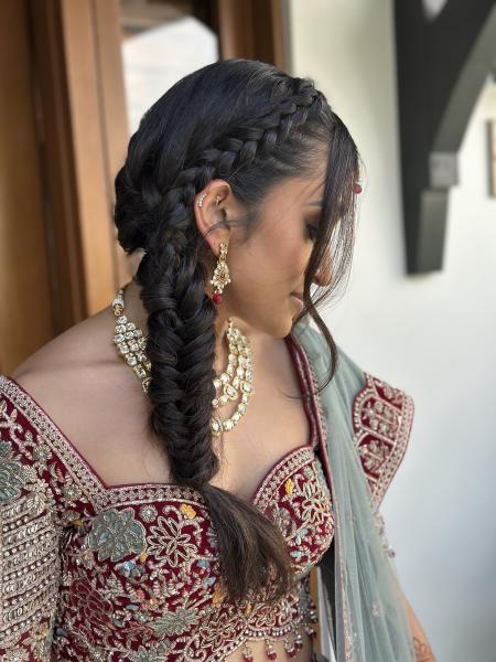 A woman in traditional Indian bridal wear looks down to the side, showing off her fishtail braid hairstyle