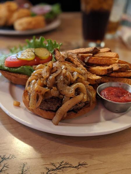 photo of a bison burger with caramelized onions and french fries served open faced on a plate