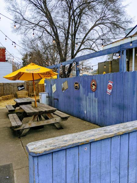 photo of a blue wooden fence and yellow patio umbrellas with picnic tables at the wunderbar in covingtin ky