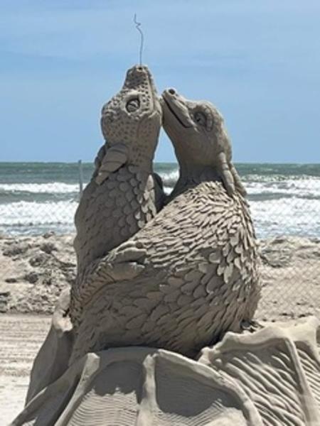 Up close of a sand sculpture showing two small dragons wrapped around each other in love.