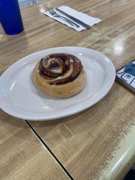 A cinnamon roll perfectly glazed sitting on a white plate at Tucci’s Family Diner.