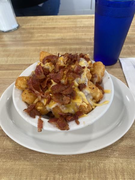 Bacon-covered tater tots in a white bowl on a white plate next to a cup of water at Tucci’s Family Diner.