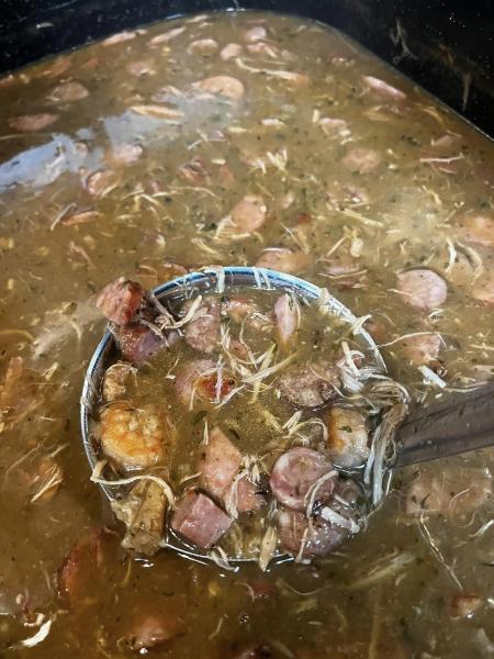 A ladle full of sausage and turkey gumbo being lifted from a large pot of gumbo