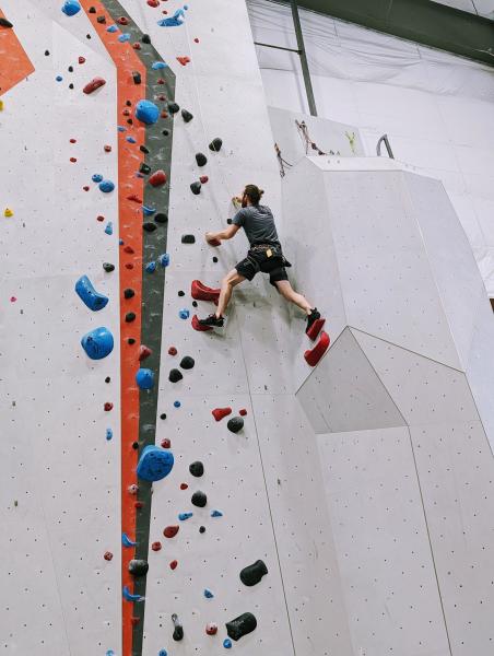 A climber scales an indoor rock wall using colorful holds at High Point Climbing and Fitness in Huntsville, Alabama.