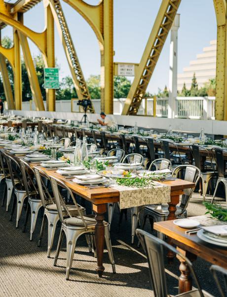 Elegantly set family-style dinner tables nestled on a yellow bridge overlooking the Sacramento river