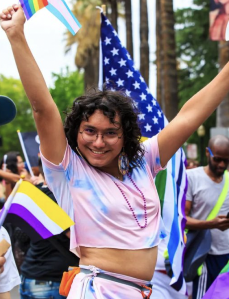 girl holding up her arms and smiling while holding a rainbow flag