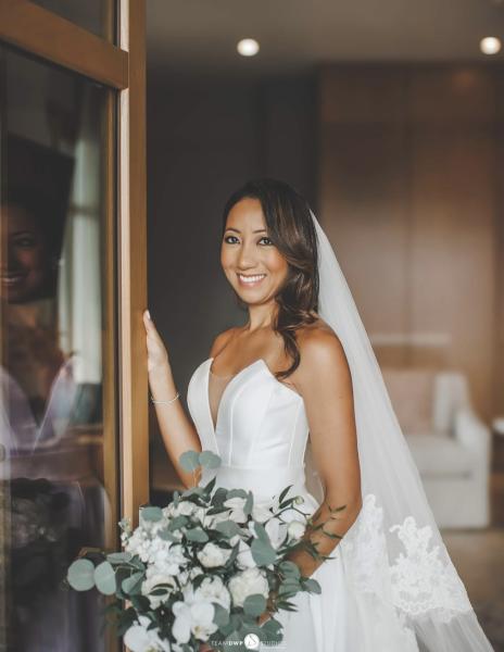 Bride smiles at the camera as she stands in doorway holding her white bouquet