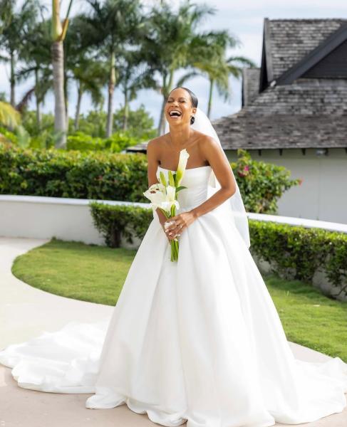 A bride laughs as she stands in a Jamaican tropical  garden holding a bouquet of long-stemmed lillies