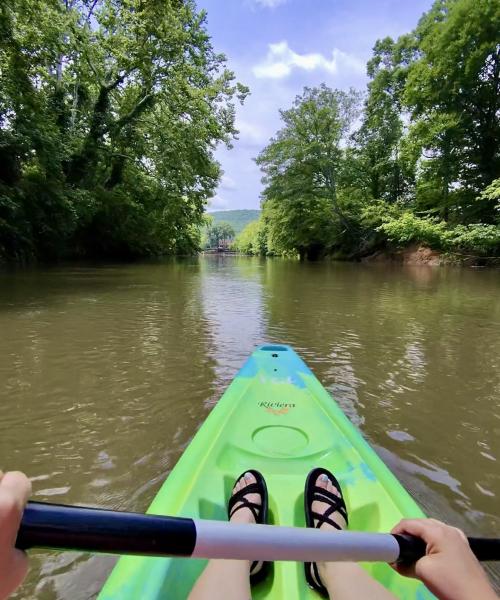 First-person view from a bright green kayak floating down the Flint River, surrounded by lush trees and calm water under a sunny sky near Huntsville, Alabama.