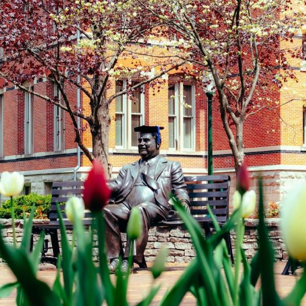 The Herman B Wells statue wearing a graduation cap on a spring day
