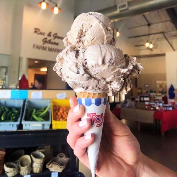 hand holding 3 scoop ice cream cone inside of farm market