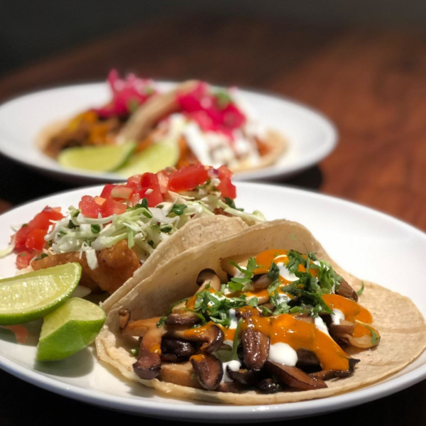 Plate of tacos made with mushrooms, garnished with sauce and served with a lime