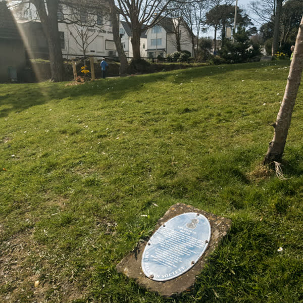 A blue plaque on a concrete plinth on the ground in a park.