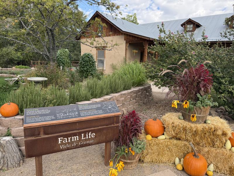A sign about Farm Life stands in front of a recreation of a farm house at the Heritage Farm at the ABQ BioPark Botanic Garden.
