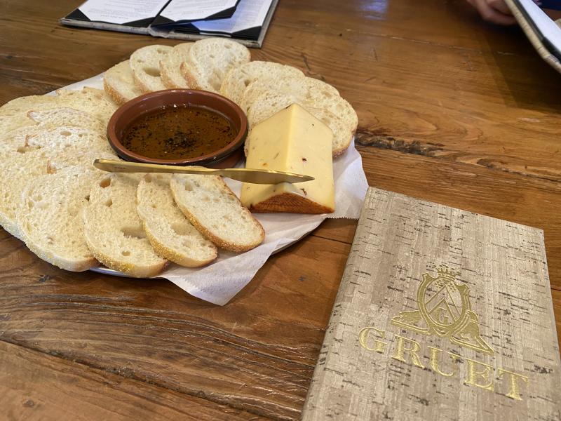 Some bread, olive oil and cheese sit on a table next to a Gruet Winery menu.